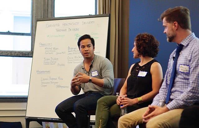 A man with a whiteboard on his behind talking to his two colleagues.