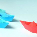 Paper boats on a surface, with one paper boat leading the others.