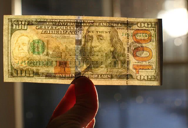 Holding a one hundred dollar bill against the sunlight close up.