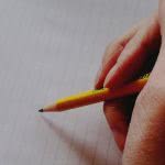 A hand holding a pencil ready to write on lined paper.