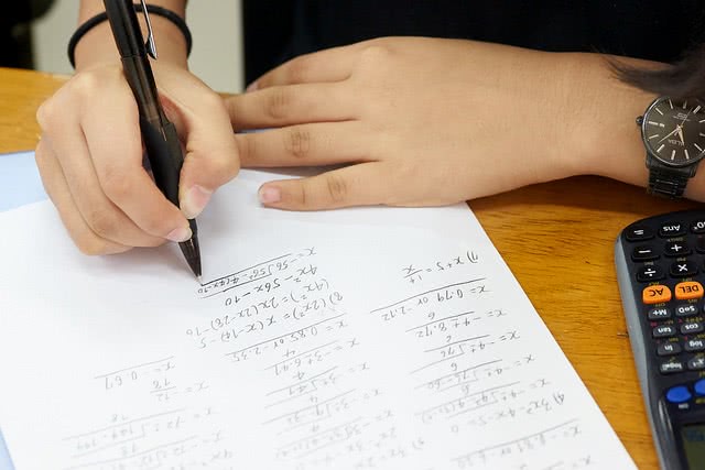 Aerial view of hand is solving a math problem on white paper with a black calculator on the desk.