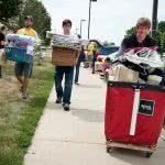 Three college students are carrying their dorm supplies while moving into college.