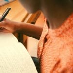 A student writing in a notebook at their desk.