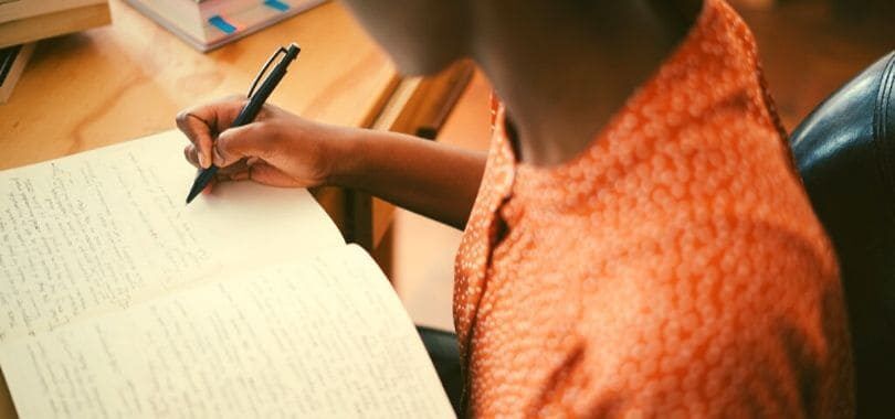 A student writing in a notebook at their desk.
