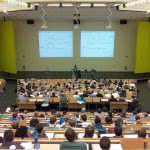 Students sitting in a huge university classroom seen from behind.