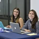 Two smiling female students with their laptops on the desk.