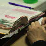 An open bible is on the desk with two hands near it.