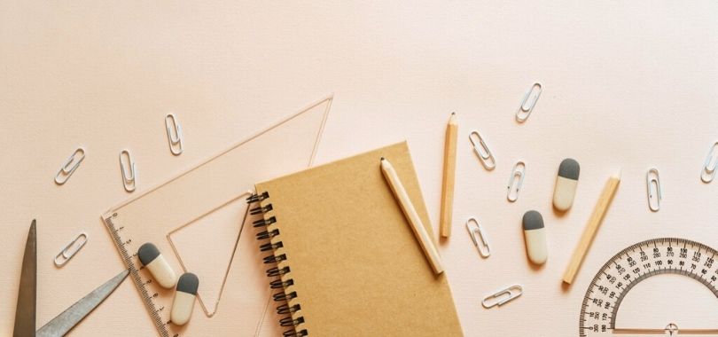 A notebook, pencils, paperclips and protractors scattered on a desk.