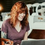 College student smiling as she works on her laptop in a coffee shop.