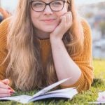 Person laying on grass with a notebook and pencil in hand.