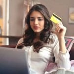 A woman sitting on a couch holding a yellow credit card.