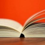 An open book on a desk with a red background.