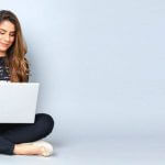 A person sitting on the ground with a laptop in their lap.