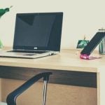 A college student's dorm desk with computer, plant, phone, and writing utensils.