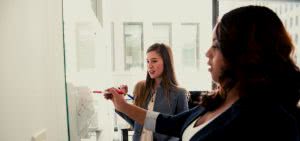 Two business administration majors writing stats on a whiteboard.