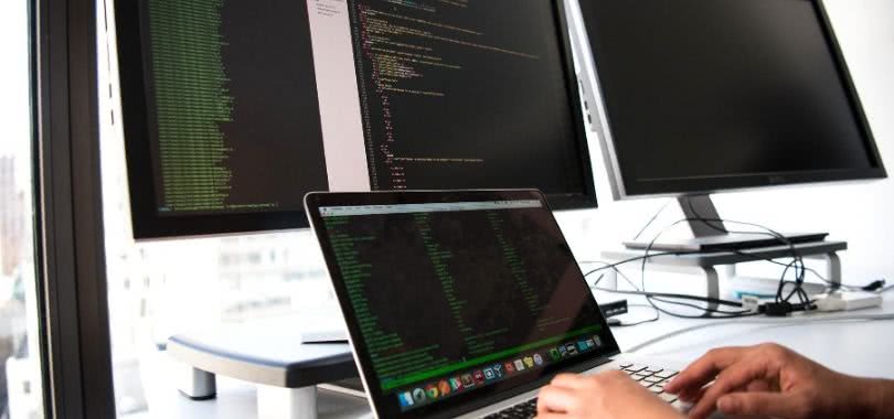 IT professional sitting at a desk with three computers.