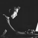 College student sitting in the dark, glaring at his laptop.