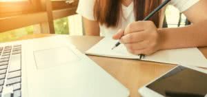 Student sitting at a desk with notebooks and a laptop studying for her SAT.