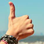 A student's hand with leather bracelets giving a thumbs up in the sky.