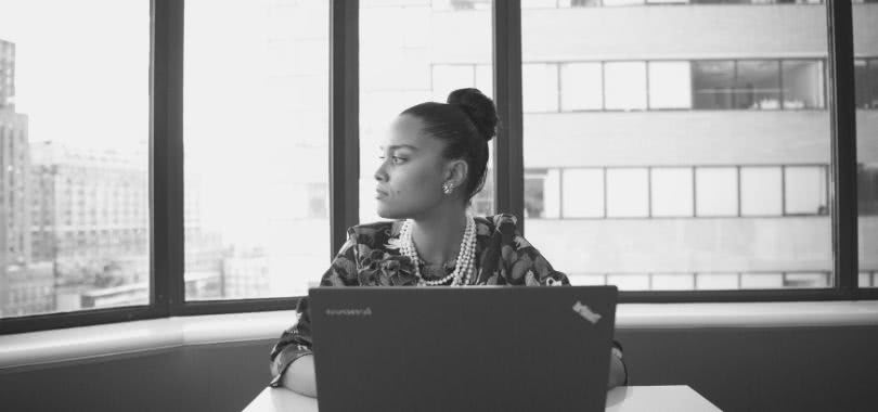 Young professional on her laptop with city skyscrapers in the window behind her.