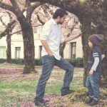 A father and young daughter standing beneath spring trees outside a college building.