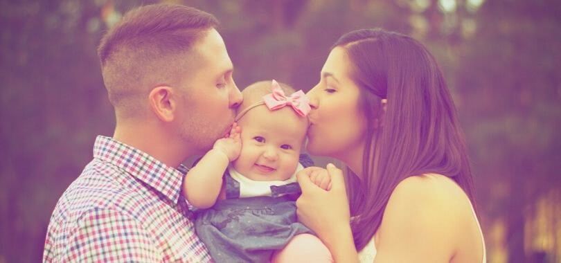 Parents kissing their baby's cheeks.