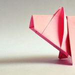 A pink origami pig standing on a gray surface.