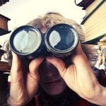 A college student surrounded by books and looking through binoculars for careers