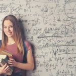 High school student with books standing in front of a whiteboard filled with math formulas.