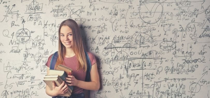 High school student with books standing in front of a whiteboard filled with math formulas.