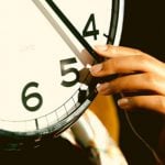 A student's hand reaches up to hold the minute-hand of a clock. They consider applying early decision for multiple schools.