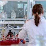 A student in a lab coat performs an experiment at her research university.