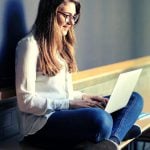 A college student sits on a desk, researching tuition insurance on her laptop.