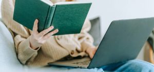 A student reads a book while a laptop rests on her legs as she studies for the SAT and ACT